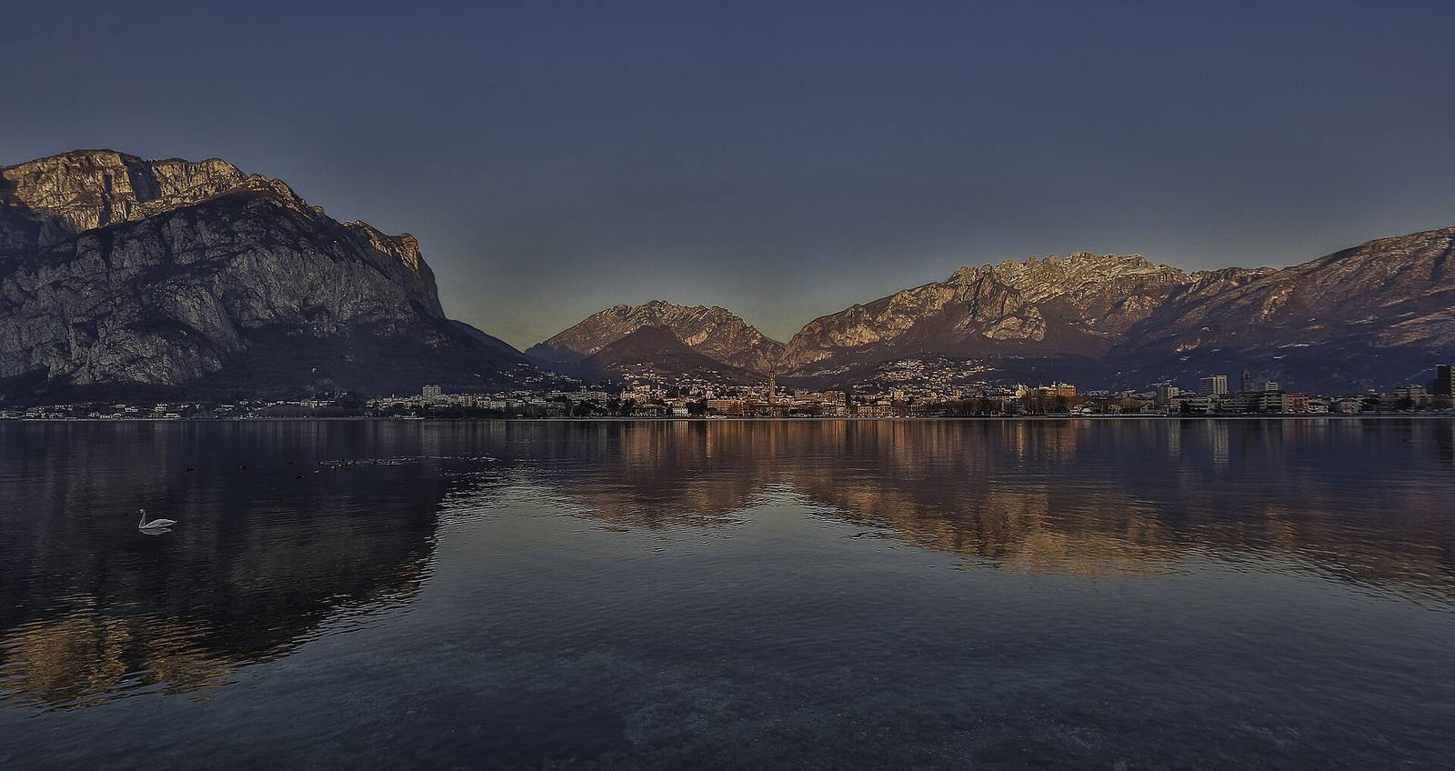 Lecco vista dal lago al tramonto, con il Resegone e le Grigne: la città ha ospitato il 14 ottobre la terza tappa del roadshow del Corpo consolare dedicato a manifattura, ricerca e innovazione.